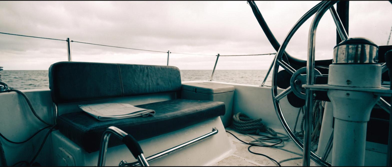 A cooler stowed beside the bench seat in the cockpit of a small cruising boat under grey sky